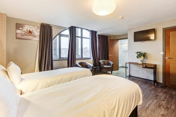 A hotel room with two beds, a desk, a chair, a TV, and a window with curtains.