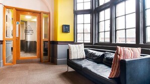 A lobby with a leather sofa, a wooden door with glass panels, and large windows. - OYO Grand Central (Liverpool)