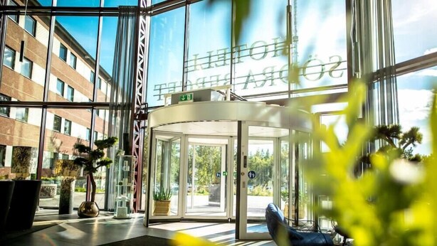 A modern hotel lobby with a revolving door, large windows, and indoor plants. - Hotell Södra Berget (Sundsvall)