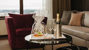 A room with a red chair, a glass table with a bottle of champagne, two glasses, and a tray with fruits. - Hotell Södra Berget (Sundsvall)