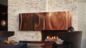A modern lounge area with a stone wall, a large abstract painting, a fireplace, and comfortable seating. - Hotell Södra Berget (Sundsvall)