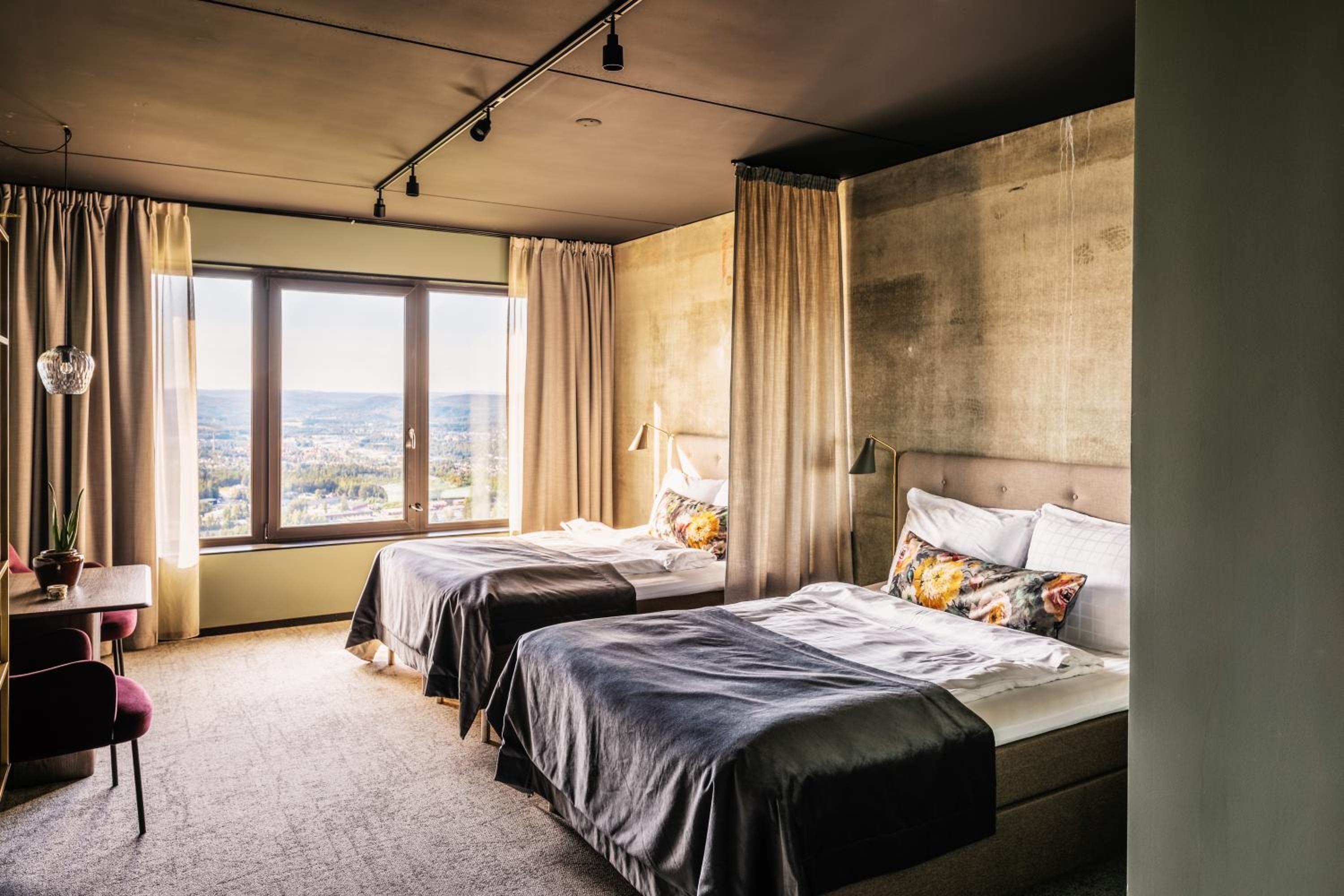 Ett hotellrum med två sängar, ett skrivbord och utsikt över staden.