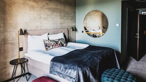 A bedroom with a bed, a round mirror, a red ottoman, and a black floor lamp. - Hotell Södra Berget (Sundsvall)