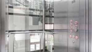 A modern elevator with glass panels and metallic interior, featuring control buttons and emergency instructions. - City Centre (Prague)