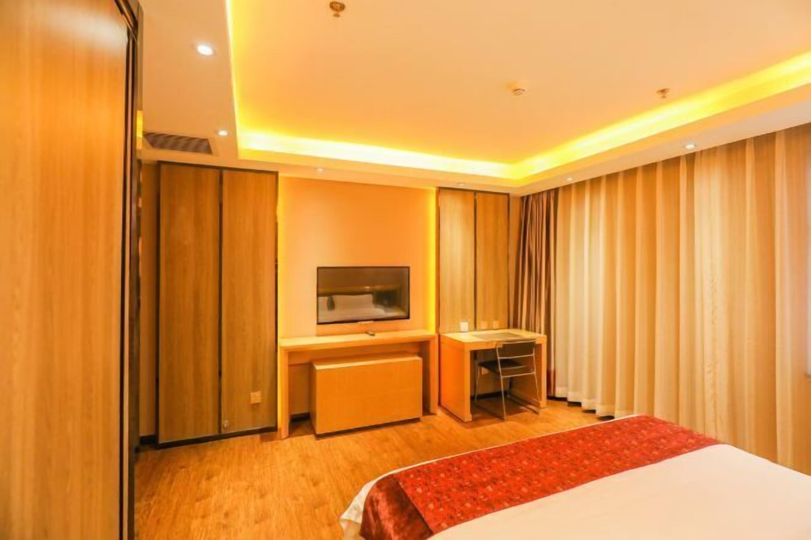 A hotel room with a bed, a desk, a television, and a window with curtains.