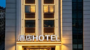 Um hotel com fachada moderna, letreiros iluminados e vários janelões.