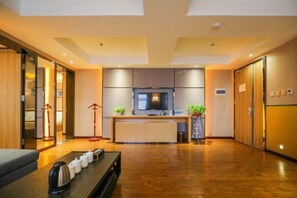 A modern hotel room with a wooden floor, a sofa, a dining table with a kettle, a TV, and a small plant. - Jinshi Building Hotel（Yuegezhuang Bridge, Beijing West Railway Station） (Beijing)