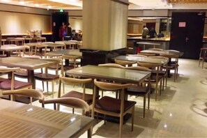 A spacious indoor dining area with multiple tables and chairs, a central pillar, and a counter in the background.