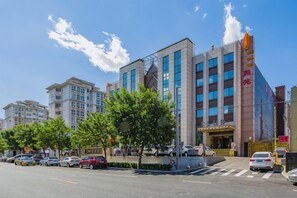 Un hotel de varios pisos con fachada moderna, una entrada destacada y un cielo despejado.