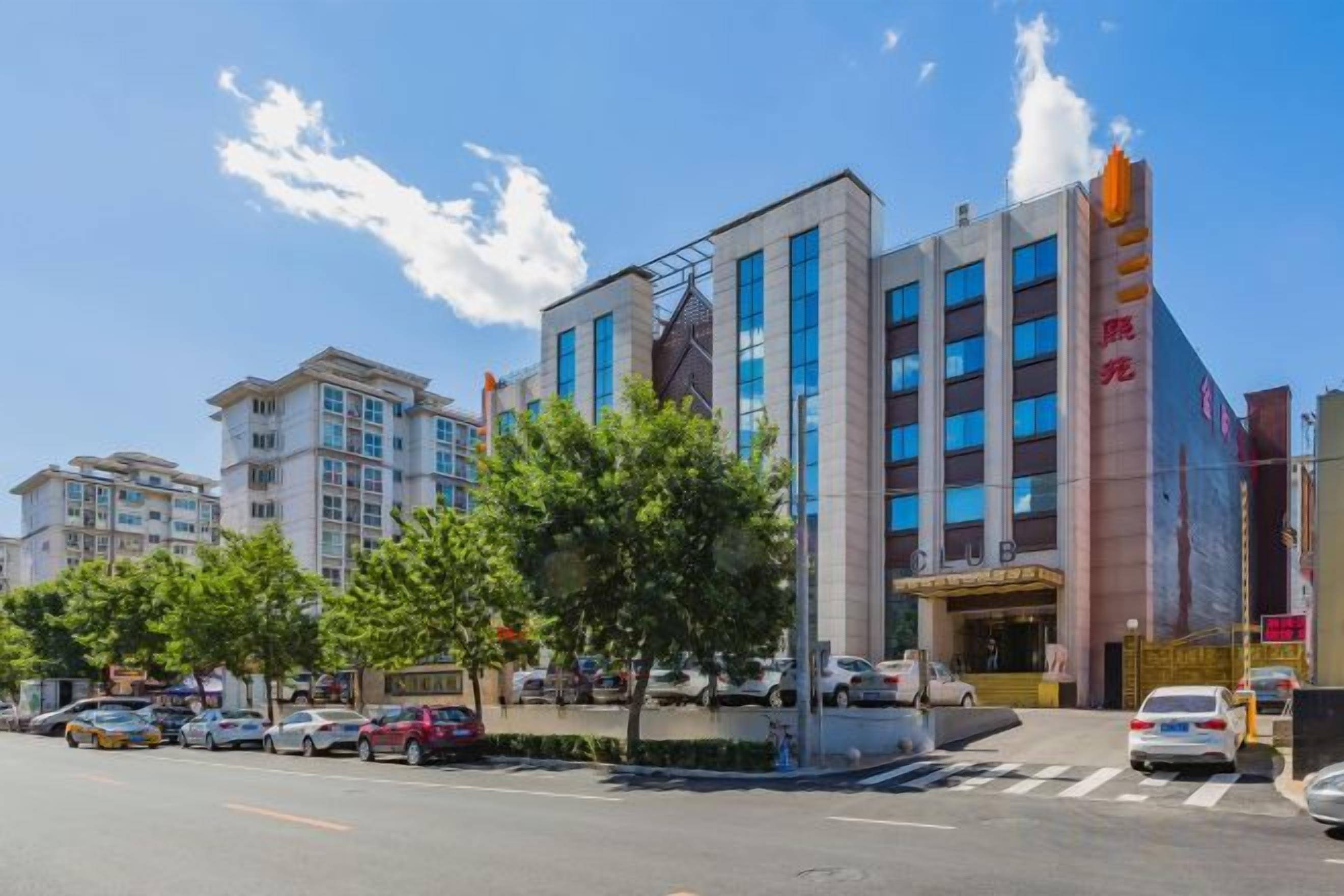 A multi-story hotel with a modern facade, a prominent entrance, and a parking area in front.