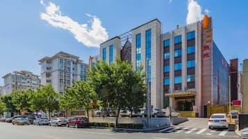 A multi-story hotel with a modern facade, a prominent entrance, and a parking area in front.