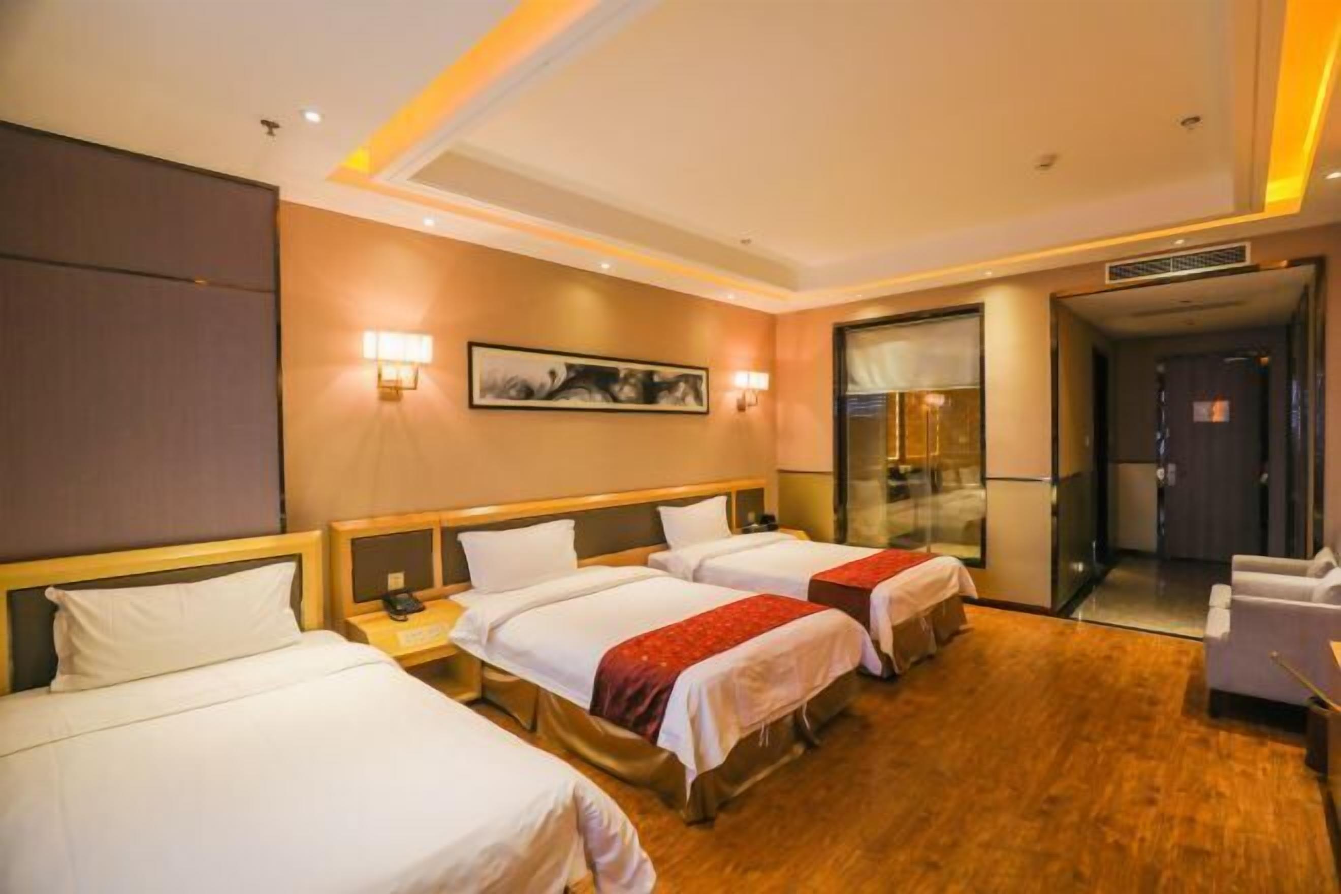 Habitación de hotel con tres camas, un escritorio, una silla y un panel de vidrio.