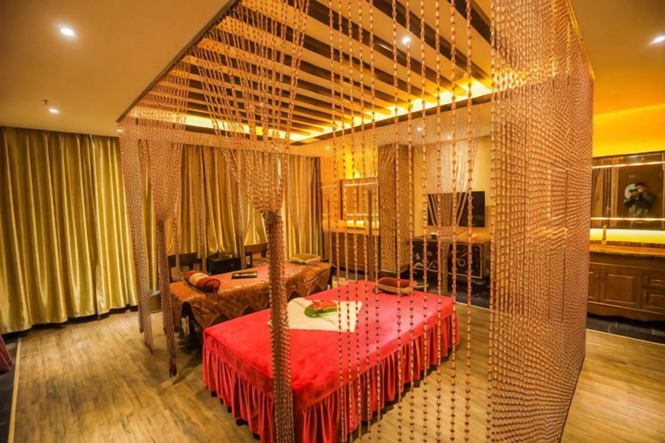 Un lit à baldaquin avec une couvre-lit rouge, un plancher en bois et un fond de scène constitué de rideaux.