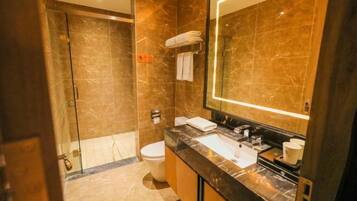 A modern bathroom with a glass shower enclosure, a marble-tiled wall, a large mirror, and a black countertop with a sink and vanity.