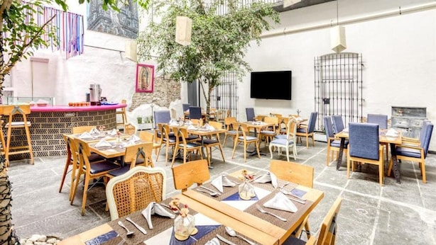 An outdoor dining area with wooden tables and chairs, a bar counter, and a TV screen mounted on the wall. - Milagro Hotel (Puebla)