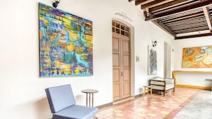 A hallway with a blue chair, a wooden door, and a large abstract painting on the wall. - Milagro Hotel (Puebla)