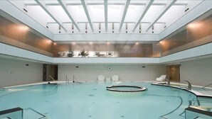 Une grande piscine intérieure dotée d’un élément circulaire central, entourée d’espaces de détente et surmontée d’un toit en verre.
