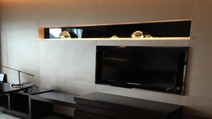 Een moderne woonkamer met een flatscreen televisie aan een muur, een donkere houten tv-kast eronder en een klein plankje erboven.