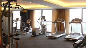 Een hotelgym met cardioapparatuur, gewichten en een groot raam dat voor natuurlijk licht zorgt.