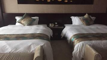 Habitación de hotel con dos camas, cada una con ropa blanca y almohadas decorativas. Se observa un mesita de noche con un teléfono y una pequeña mesa entre las camas. La habitación tiene un cabecero oscuro con adornos circulares.