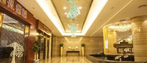 A hotel lobby with a marble floor, a reception desk, a grand piano, and a decorative chandelier.