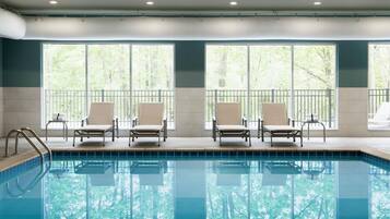 Une piscine avec quatre chaises longues et de grandes fenêtres donnant sur la forêt.
