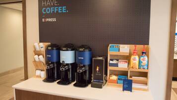 A coffee station with four coffee makers, a hot water dispenser, and a display of coffee creamer bottles.