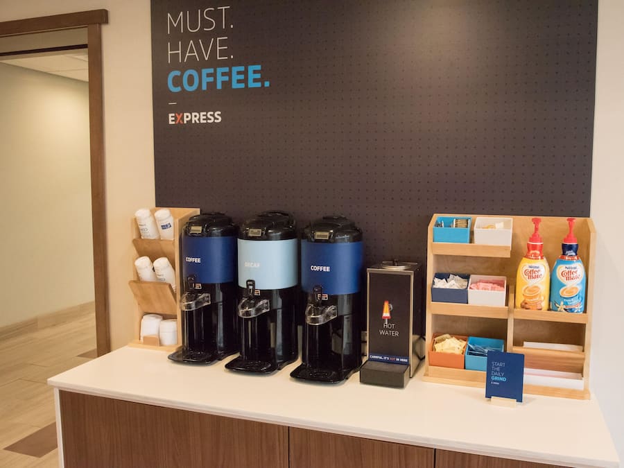 A coffee station with four coffee makers, a hot water dispenser, and a display of coffee creamer bottles.