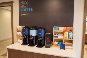 Un espace dédié au café, équipé de quatre machines à café, d’un distributeur d’eau chaude et d’un présentoir contenant des bouteilles de crème à café.