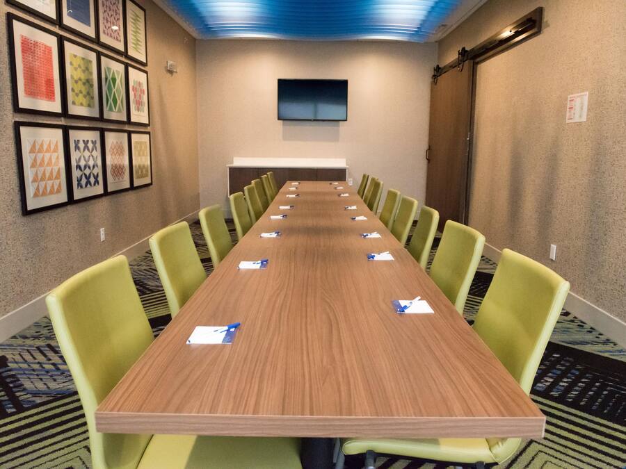 Una sala conferenze con un lungo tavolo, sedie verdi e quadri appesi alle pareti.