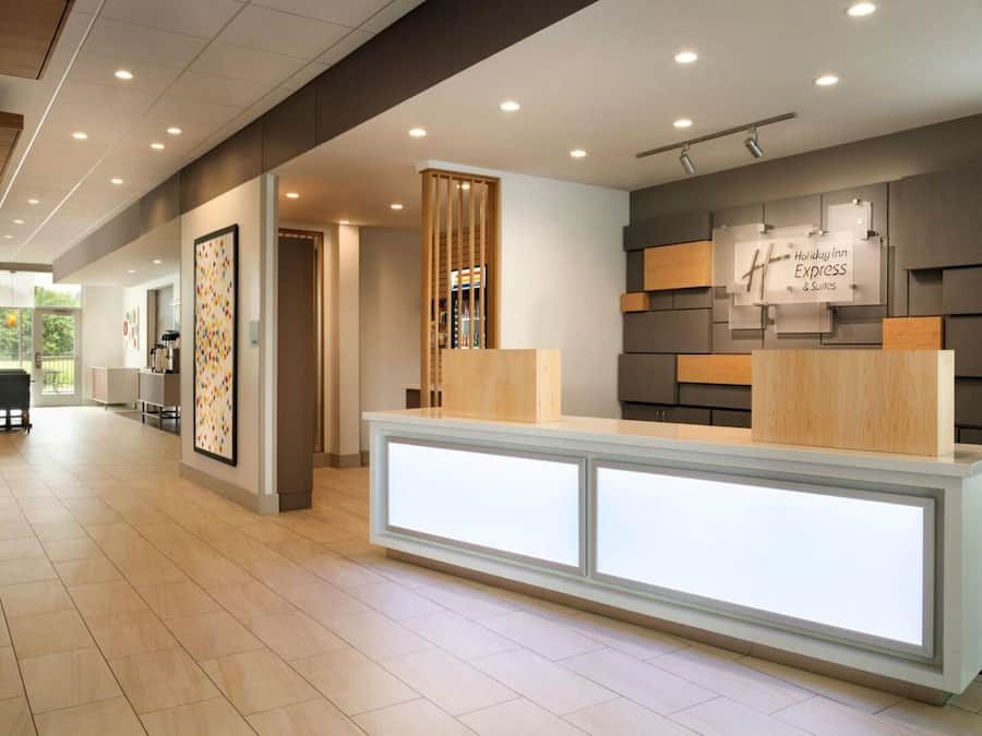 A modern hotel reception area with a reception desk, a sign for Holiday Inn Express & Suites, and a view of the outdoors.