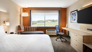 Habitación de hotel con una cama grande, un escritorio, una silla, un televisor y una ventana con vistas al exterior.