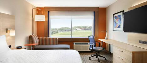 Habitación de hotel con una cama grande, un escritorio, una silla, un televisor y una ventana con vistas al exterior.