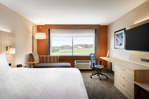 Une chambre d’hôtel avec un grand lit, un bureau, une chaise, une télévision et une fenêtre donnant sur l’extérieur.