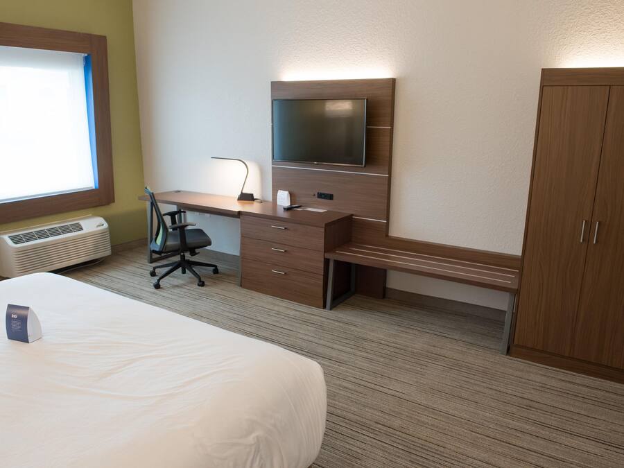 A hotel room with a bed, a desk with a chair, a TV, and a wardrobe.