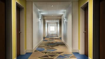 A long, narrow hotel corridor with multiple doors on either side, a patterned carpet, and a ceiling with recessed lighting.
