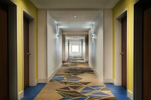 Un largo pasillo de hotel, estrecho, con varias puertas a ambos lados, alfombra estampada e iluminación empotrada en el techo.