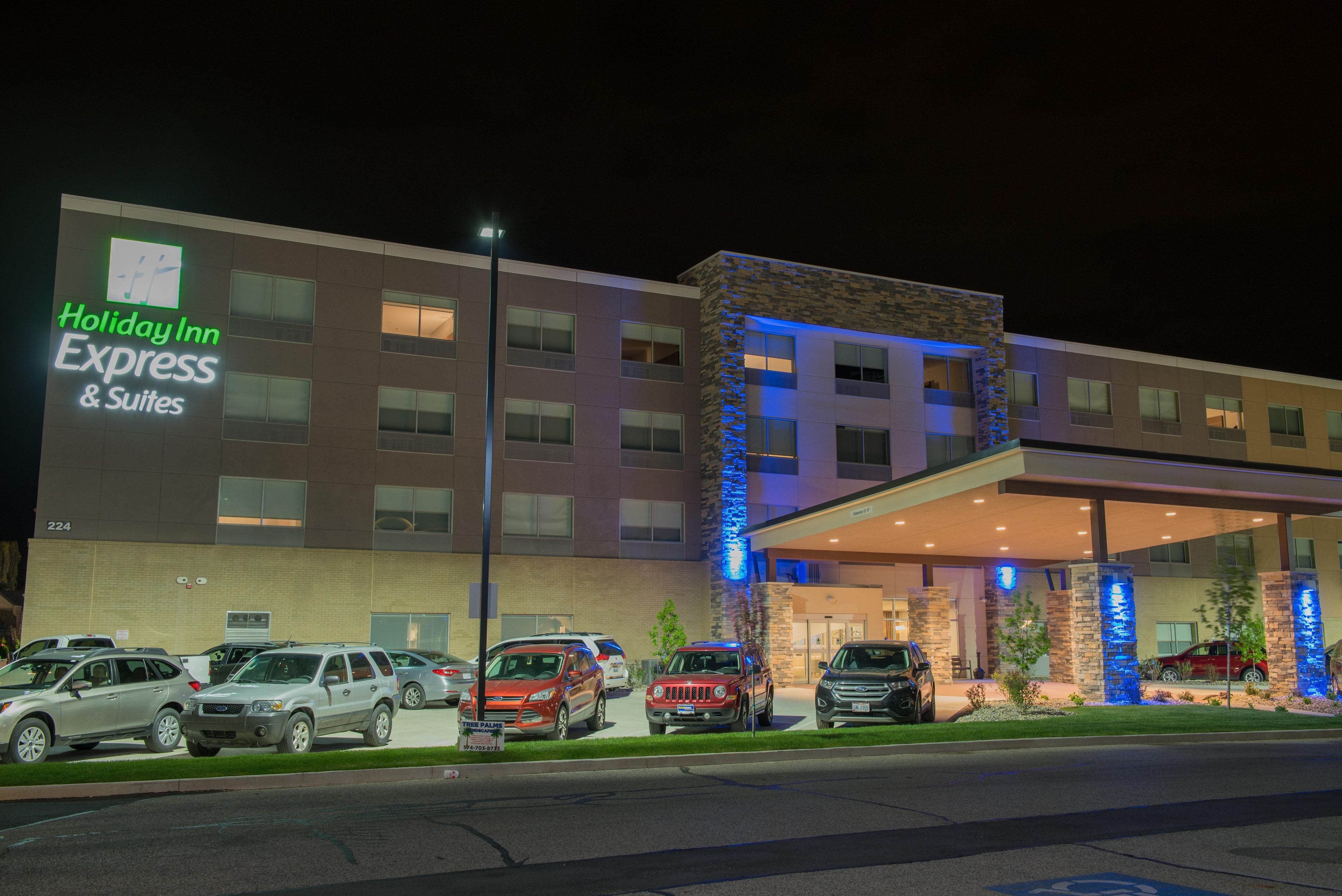 A Holiday Inn Express & Suites building with a modern design, featuring a parking lot with several cars and a well-lit entrance.