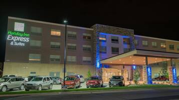 A Holiday Inn Express & Suites building with a modern design, featuring a parking lot with several cars and a well-lit entrance.
