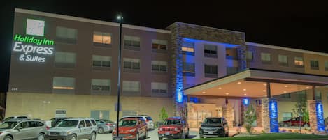 A Holiday Inn Express & Suites building with a modern design, featuring a parking lot with several cars and a well-lit entrance.