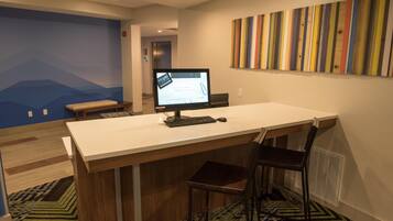A modern office space with a desk, two chairs, a computer monitor, and a colorful striped wall art piece.