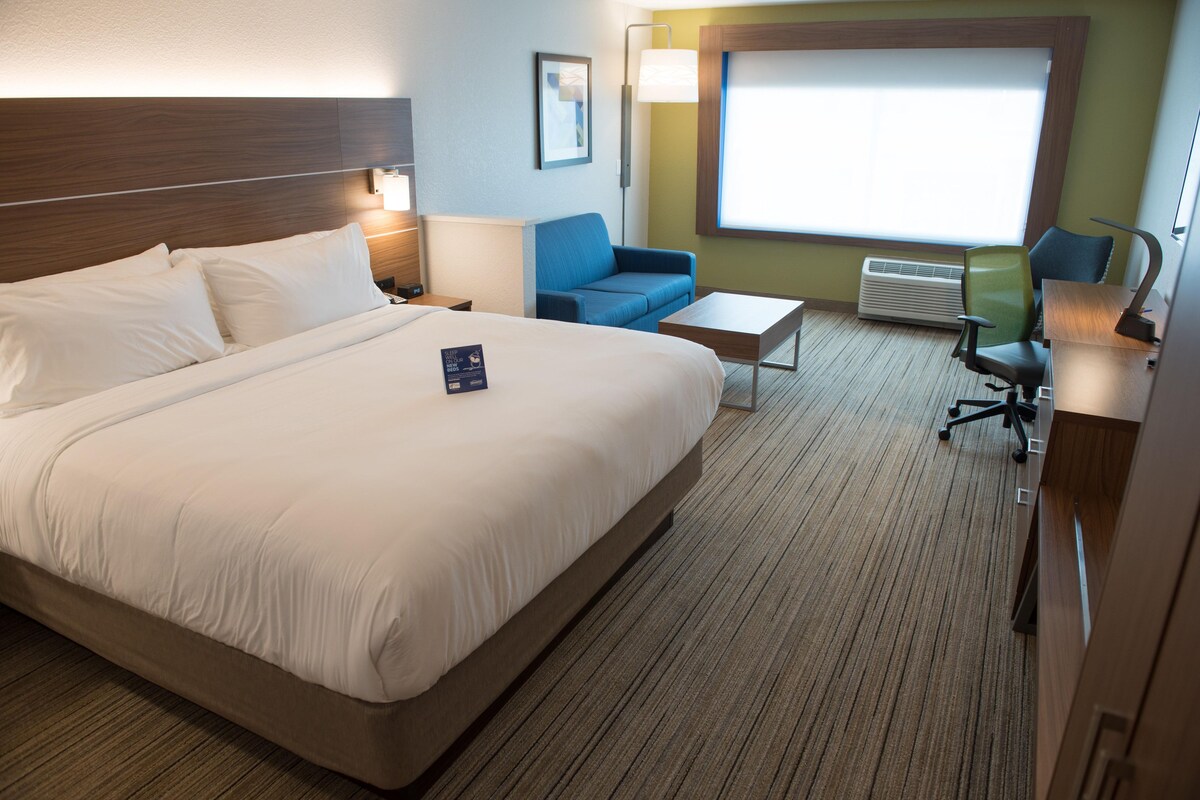 Un cuarto de hotel con una cama grande, un escritorio, una silla y un ventanal con vistas.