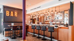 A modern bar area with a wooden counter, multiple bar stools, and a 'BAR' sign. - Premier Inn Munich Airport Sud Hotel (Hallbergmoos)