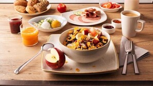 A breakfast setting with various dishes, a coffee cup, and a bottle of milk on a wooden table. - Premier Inn Munich Airport Sud Hotel (Hallbergmoos)
