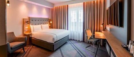 A hotel room with a bed, bedside tables, a desk, a chair, and a TV.