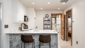 A modern kitchen with a white countertop, two bar stools, and patterned backsplash tiles.