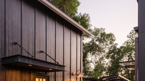 A modern building with a dark wooden facade, a large door with a window, and a metal staircase leading to an upper level.