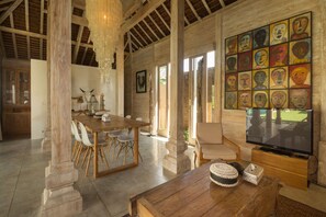 A spacious room with a wooden dining table, chairs, a television, and a wall with colorful artwork. - The Complete Guide to Renting Your Exclusive Holiday Villa in Kerobokan with Private Pool and Fully Staffed (Bali)