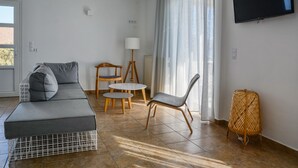 A modern living room with a grey sofa, two wooden tables, a wicker chair, and a TV mounted on the wall.