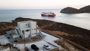 A modern building with a flat roof and a carport, overlooking a calm sea with a ferry passing by.